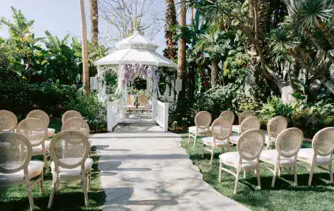 An outdoor wedding ceremony setup with a flower draped gazebo and rows of chairs flanking the isle
