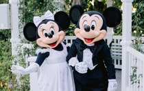 Bride Minnie Mouse and groom Mickey Mouse standing arm in arm in front of an outdoor gazebo