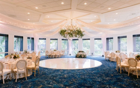 A circular room featuring tall windows, round tables, drapery and a dance floor