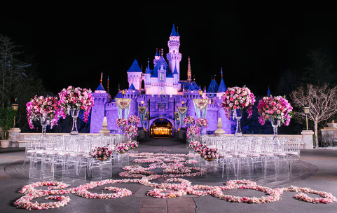 Sleeping Beauty Castle is lit up at night and surrounded by chairs and elegant floral displays