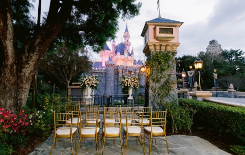 Chairs and florals are set up for a wedding ceremony in front of Sleeping Beauty Castle