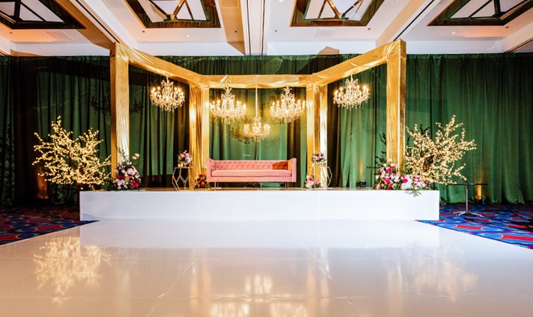 A dance floor in front of a raised platform with a couch and several bouquets under chandeliers