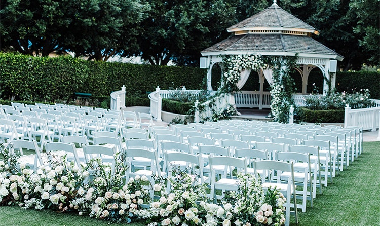 Several rows of chairs facing a gazebo lined with roses