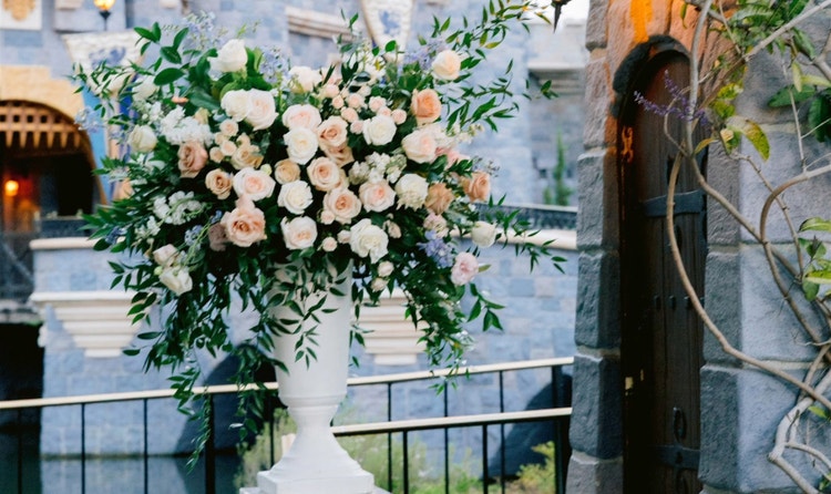 A flower arrangement elevated on a pedestal, illuminated by a hanging lantern, next to Sleeping Beauty Castle