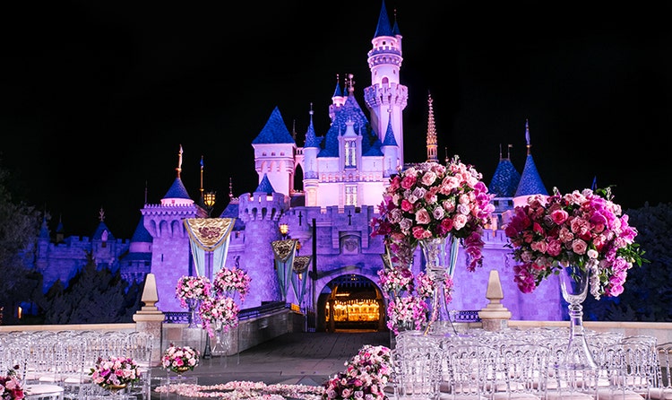 Large bouquets in clear glass vases and translucent chairs arranged for a wedding in front of a castle