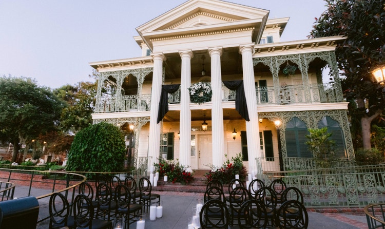 The Haunted Mansion with ornate ironwork balconies and rows of ceremony chairs with candles at dusk
