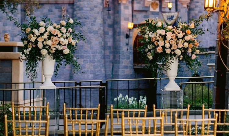 Two sections of chairs pointed towards a center area decorated with ornate flower arrangements in vases facing Sleeping Beauty Castle