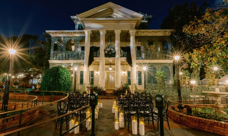 The Haunted Mansion with columns and ornate balconies illuminated for an evening wedding ceremony with candles