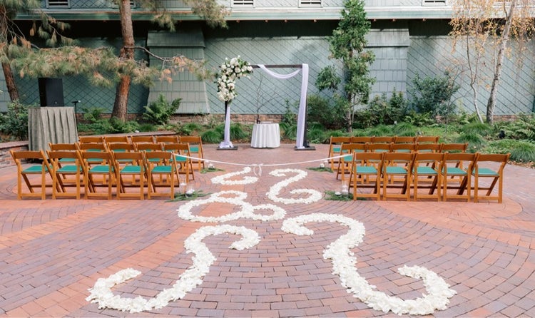 Rows of chairs along a flower covered aisle leading to an arch in a courtyard