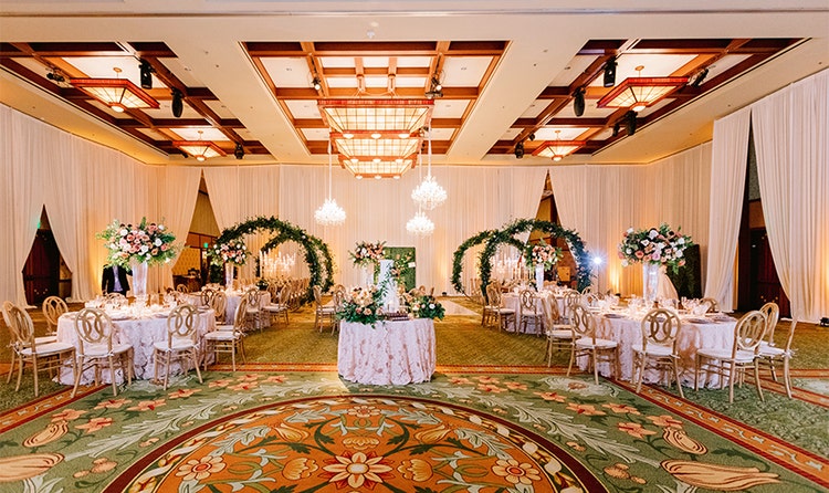A ballroom featuring flower arches, high ceilings, curtains and flower centerpieces