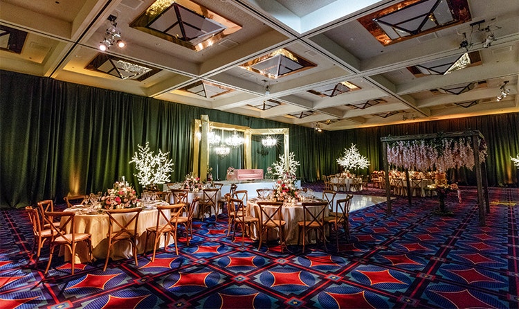 Several round tables near a dance floor, a raised platform with a couch and an archway