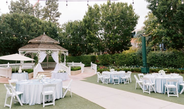 In an open garden area, 3 dining tables are set for a formal occasion
