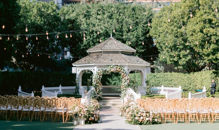Rows of chairs pointed toward a wedding gazebo decorated with floral arrangements in Rose Court Garden