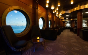 An upscale lounge with dark wood paneling, bar seating and intimate booth seating areas at Keys aboard the Disney Magic
