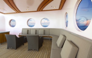 A lounge area surrounded by porthole windows with views of the ocean on a Disney cruise ship