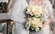 Two women in formalwear hold matching bouquets as they smile and gaze into each other's eyes
