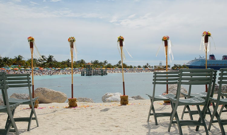 A line of tiki torches on the edge of a beach and a Disney Cruise Line ship in the water