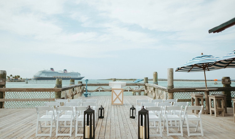 Pier wedding ceremony setup with lanterns lining the wooden aisle and a view of the Disney cruise ship at sea
