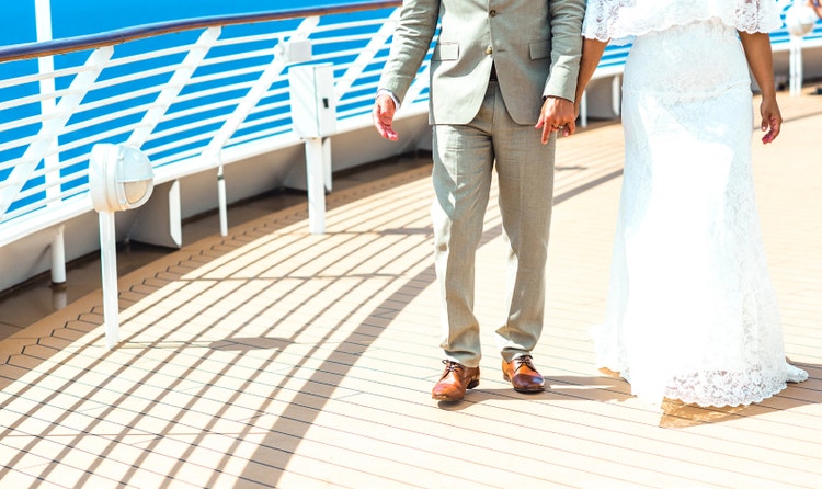 A bride and groom holding hands while walking on the top deck of a Disney cruise ship