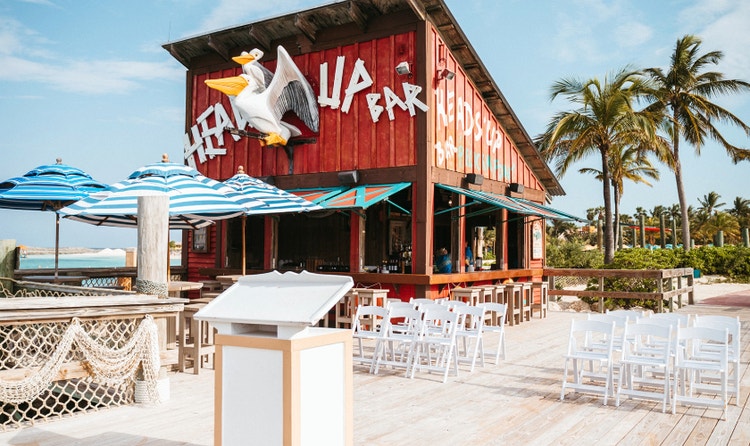 A pier wedding setup with a lectern and chairs next to a wedding reception area at the Heads Up Bar with a pelican design