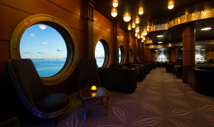 Tables next to a row of porthole windows at Keys, a piano bar on the Disney Magic.