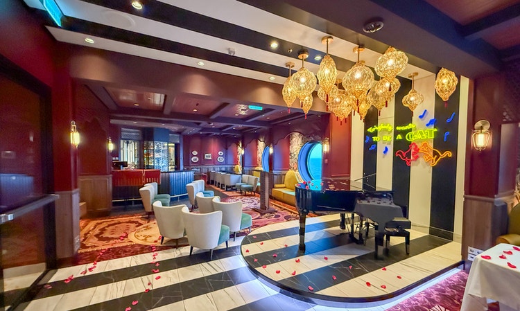 A woman playing the piano next to 2 bartenders at Scat Cat Lounge aboard the Disney Treasure