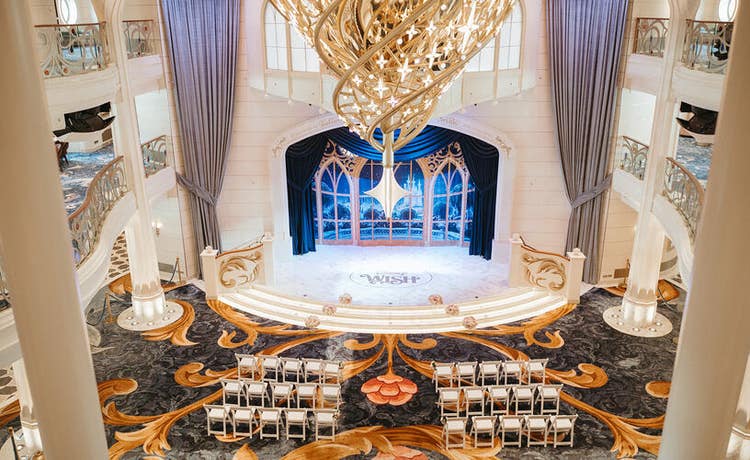 An aerial view of a lavish atrium set for a wedding ceremony aboard a Disney cruise ship with rows of chairs and floral arrangements flanking an aisle