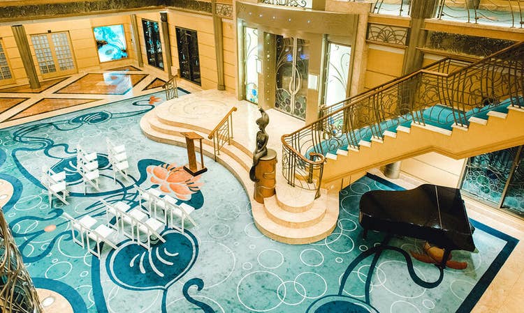3 rows of chairs facing a podium on The Atrium floor, and a grand piano sit near a grand staircase