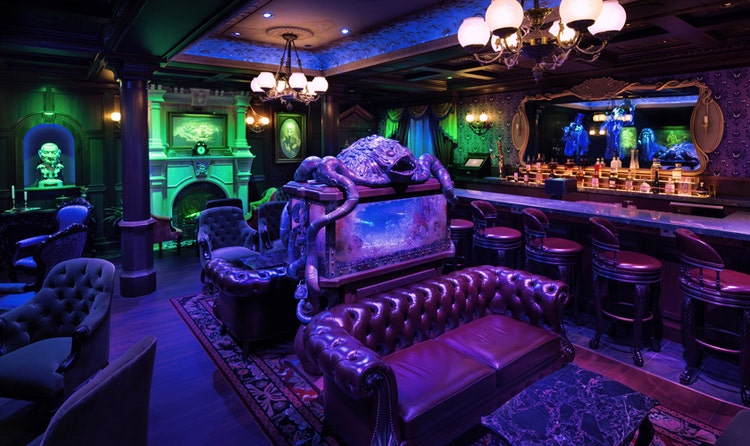 The Haunted Mansion Parlor aboard the Disney Destiny featuring an eerie Victorian lounge with a bar, leather chairs and sofas, and a fish tank topped with a sea monster