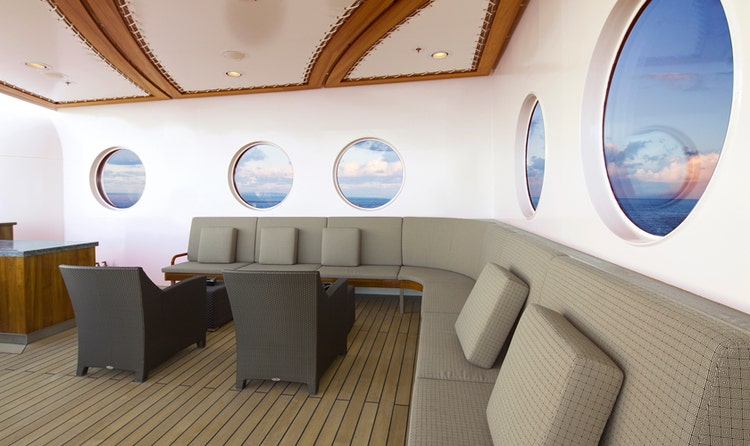 A lounge with a large, curved sofa, bar and chairs on the Disney Dream
