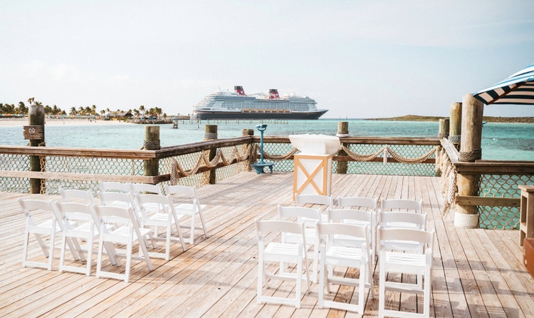 Waterfront wedding ceremony space on a wooden pier with decorative rope netting, chairs and a view of a cruise ship
