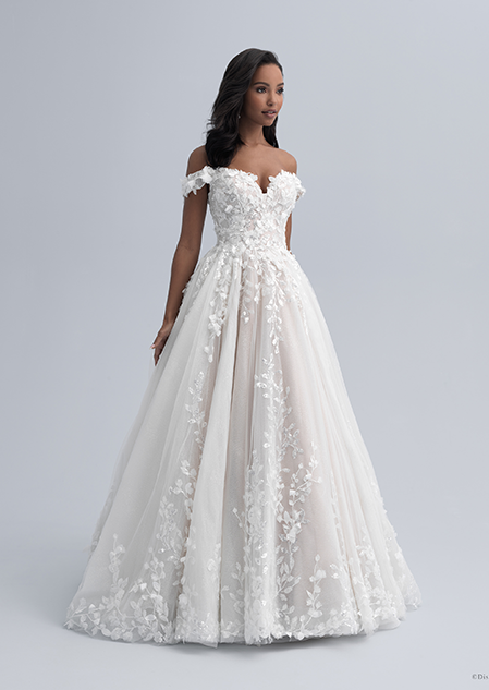 A woman wearing a wedding dress with an off the shoulder neckline and flowers adorning the bodice and extending down the skirt