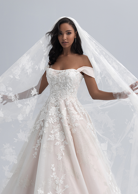 A bride wearing an off the shoulder wedding dress with straps hanging above her elbows and a large lace veil