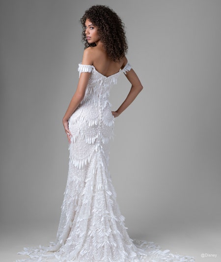 The back of a bride wearing a Tiana inspired sheath gown featuring off the shoulder sleeves, a train and light fringe detail