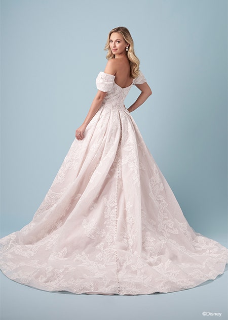 A bride wearing an Aurora inspired A line wedding gown featuring embroidery and off the shoulder sleeves