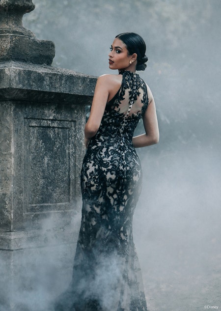 A woman posing by a stone structure with her back turned wearing a fitted gown with intricate lace details