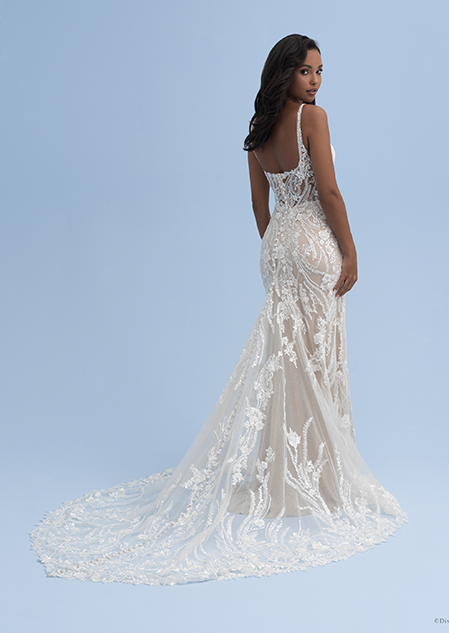 A bride looks over her shoulder while wearing a wedding dress with straps and crystal flowers extending down the train