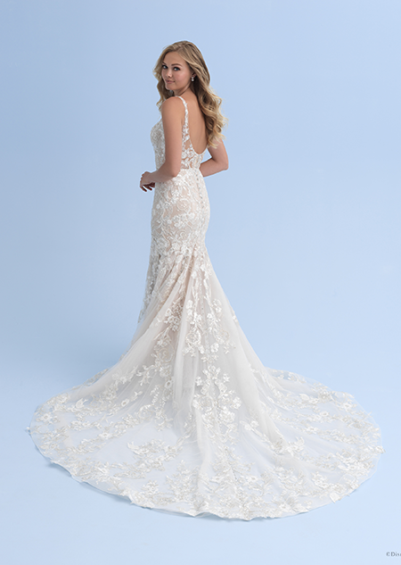 A side view of a woman in a form fitting wedding dress with a strap across her shoulder and beaded crystal flowers going down the train