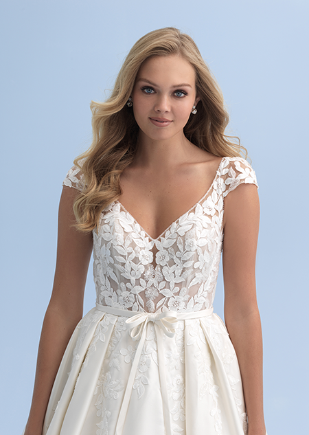 A close up of a woman in a wedding dress with cap sleeves and a partially see thru bodice with a belted waist