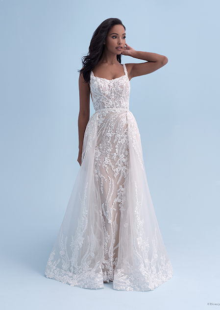 A bride in a form fitting wedding dress with a square neckline decorated with crystal flowers, with additional layers added onto the sides of the skirt