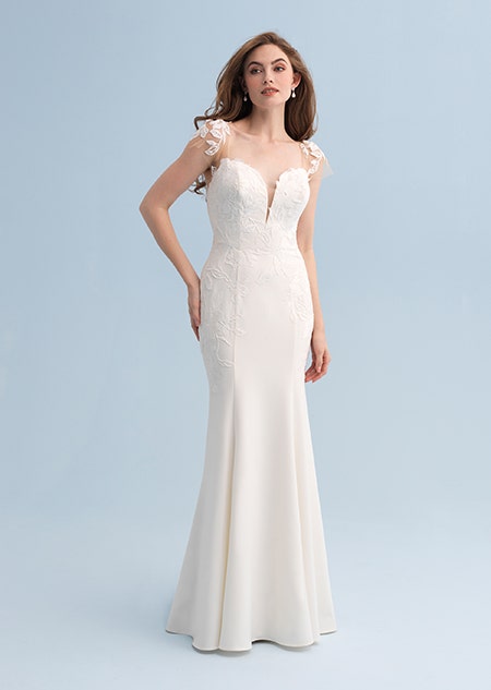 A woman wearing a form fitting wedding dress with a leaf design across the shoulders