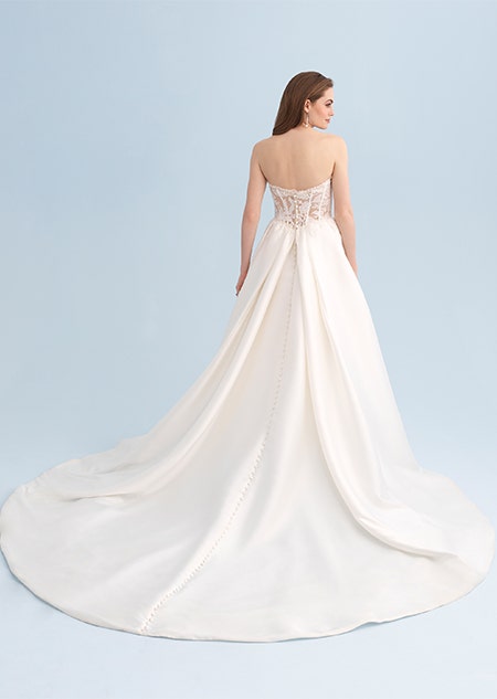 A woman looking over her shoulder wearing a strapless wedding dress with a long trail