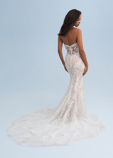 A woman looking over her shoulder wearing a form fitting and lacy strapless wedding dress