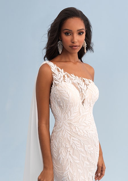 A woman wearing a form fitting wedding dress with a lace leaf pattern and asymmetrical sleeves