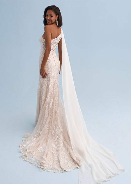 A woman wearing a form fitting wedding dress with asymmetrical sleeves connected to the trail
