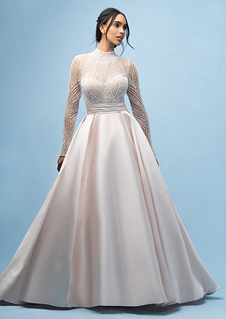 The front of a bride wearing a Jasmine inspired ball gown featuring an illusion neckline, a sheer beaded bodice and long sleeves