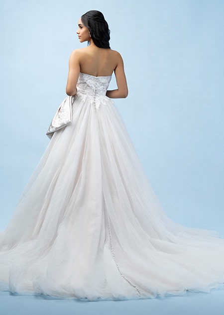 The back of a bride wearing a Snow White inspired A line gown featuring a beaded bodice, a train, floral designs and an off center bow at the waist