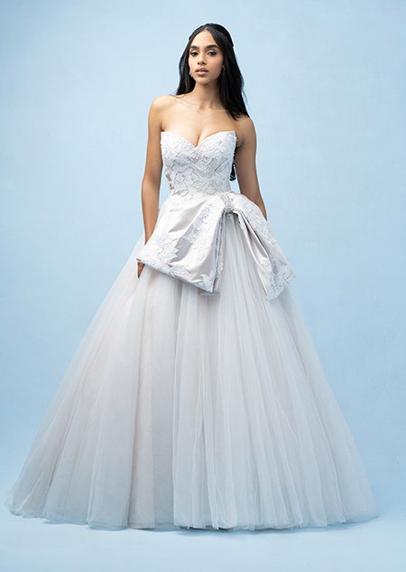 The front of a bride wearing a Snow White inspired A line gown featuring a sweetheart neckline, a beaded bodice, floral designs and an off center bow at the waist