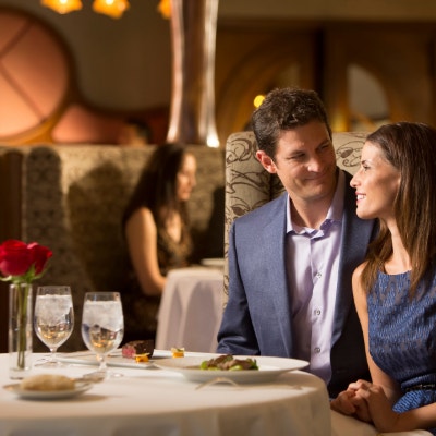 A man and a woman smile at each other while sitting in a plush booth at Remy