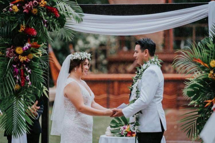 bride and groom, couple, wedding ceremony, ceremony, altar area, altar floral, altar decor, tropical floral, tropical, flower crown, lei, white drape, exchanging vows, vows